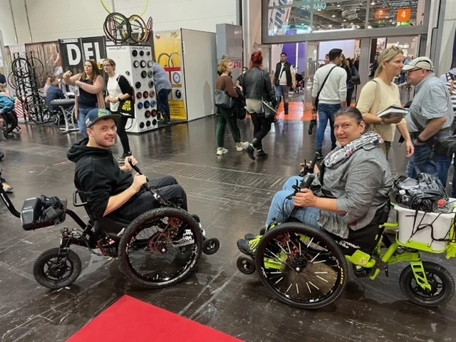 Customers seated in Mountain Trike all terrain wheelchairs in an exhibition hall